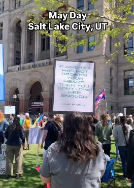 A woman is standing at the Utah State Capitol with a bunch of other protesters. She's facing away from the camera and holding up a sign that says "IF AMERICA HAS NOT BROKEN YOUR HEART THEN YOU DON'T LOVE HER ENOUGH." -Cory Booker