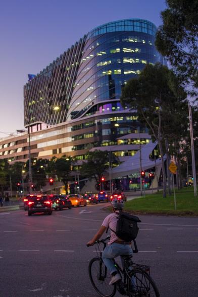 A biker pauses at a large roundabout in purple sunset lighting in front of a tall curved building