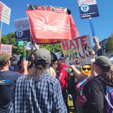 May Day 2025 in Cal Anderson Park in Seattle. A crowd of people with signs. Many of them are using their signs to cover up an obnoxious Christian zealot creep's sign.