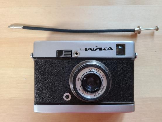 A photo of a small Russian film camera. It looks very much like any small mid 20th century camera; it has Russian writing on top. There is a small cable above it, that is an elegant but very short remote shutter cable.