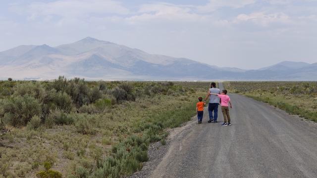 A man walks with two kids on a dirt road in the middle of a desert.