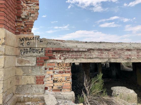 Part of the foundation with a view into the basement of the old school. Some graffiti reads, "Welcome to paradise."