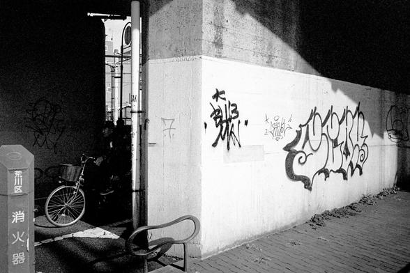 A cyclist emerges from the darkness behind a graffiti covered wall