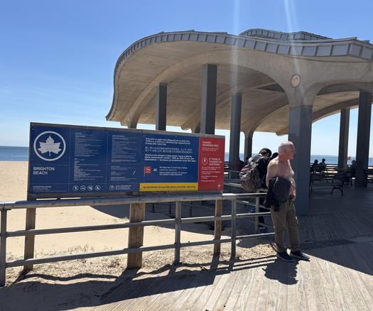 NYC Parks sign, Brighton Beach Park, also someone standing nearby and the roof shelter in the background.
