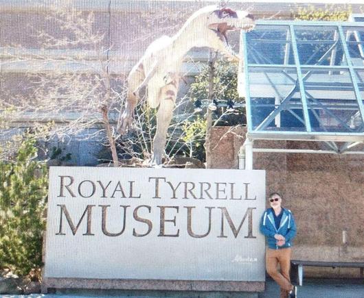 The image shows the large Royal Tyrrell Museum sign with a figure of a dinosaur on top of it and standing beside it is the poster Stefano Landi.