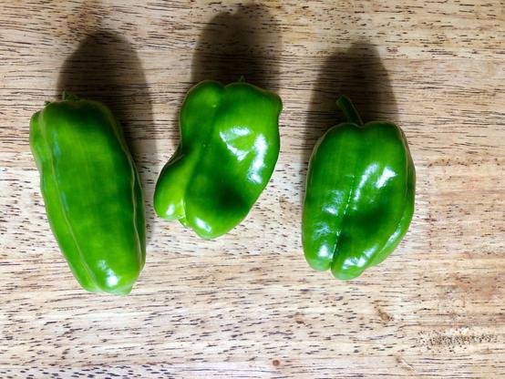 Three homegrown green peppers on a wooden table.