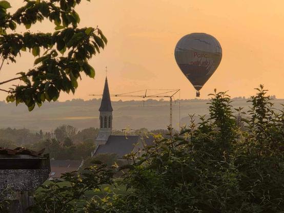 Une photo aux teintes orangées. Une église, une montgolfière proche de l’église et entre les deux, une grue.