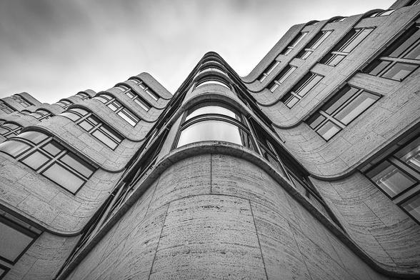 Look-up black and white shot at a long exposure on the facade of a modern building in shape of a wave on a grey cloudy day in Berlin.