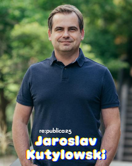Fotos von Jaroslav Kutylowski. Er trägt kurze Haare und hat seine Hände in den Hosentaschen. Er trägt ein Poloshirt und lächelt in die Kamera. Im Hintergrund sind verschwommen Bäume zu sehen.
