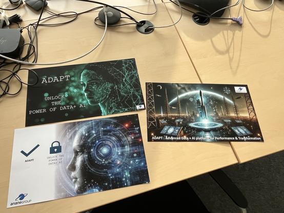 Three promotional materials are displayed on a table. The first poster features a digitally rendered female face with a circuitry design and the text "ADAPT" and "Unlock the Power of Data + AI." The second poster prominently displays the same theme with a visual