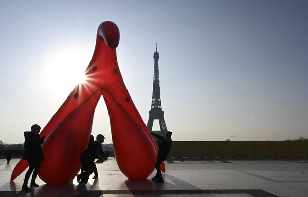 un clitoris gonflable rouge érigé dans le soleil levant devant la tour Eiffel et aussi grand qu’elle