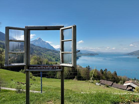An open window on poles on a meadow with a mountain visible though the window and a lake on the right of the window.