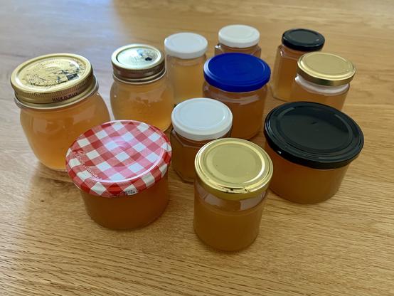 Eine Sammlung von Gläsern, die mit Tannenspitzgelee gefüllt sind und auf einem Holztisch ausgestellt sind. Die Gläser variieren in Größe und Farbe, einige haben dekorative oder gemusterte Deckel.