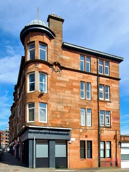 A red sandstone corner tenement on a Glasgow street.