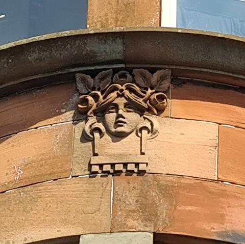 A relief sculpture of a female face surrounded by flowers abd leaves.