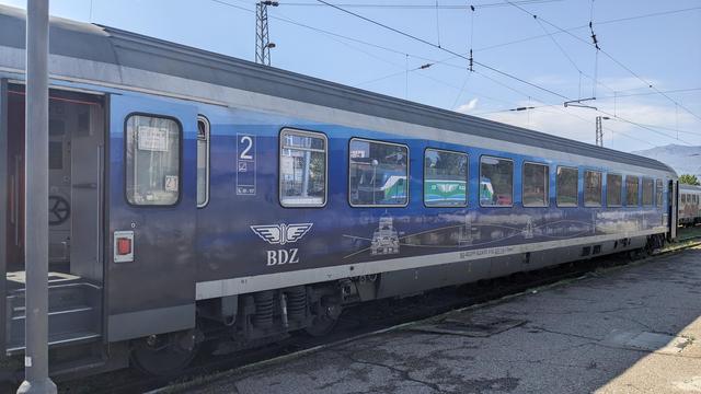Outside of a modern BDŽ RIC coach in a livery with a blue gradient and sights of different cities.