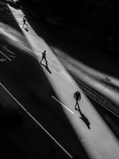 en ville, un rayon de soleil entre les immeubles dessine un couloir sur la chaussée, trois hommes l’empruntent comme un passage piétons