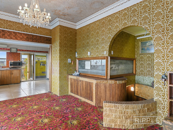 Buckle up. Inside a house, empty of furniture. A wide doorway at the back of the room shows the kitchen, with cream tiles on the floor and wooden doors on the cupboards. Next to the door leading outside is a shower room tiled in bright yellow.
The room the photographer is in has gold flocked wallpaper in a busy design. The carpet is swirling shades of red and purple, with gold sunbursts. Above the doorway there is a panel of bronze circles. A small chandelier hangs from a stained ceiling. An arch shaped door way in the side wall leads to a circular staircase down, with a low wall at the top to stop you falling down it while blinded by the carpet. At the top of the staircase, is a fish tank built into the wall, framed in wood. It's currently both empty and filthy.