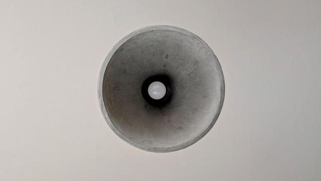 Concrete ceiling lightshade viewed direct from beneath, with lightbulb in the centre. Appears abstract