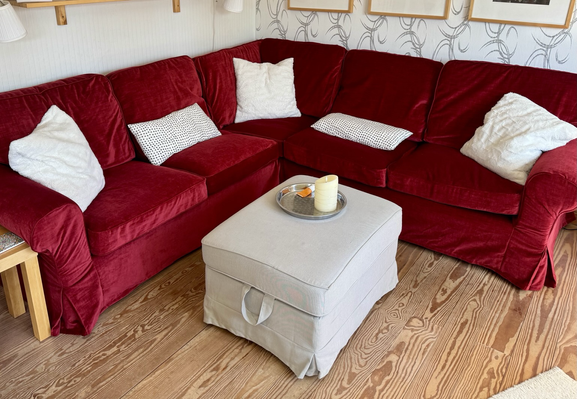 Rotes Ecksofa mit roten Bezügen, weißen Kissen und einem beigen Polsterhocker. Sieht aus wie neu.