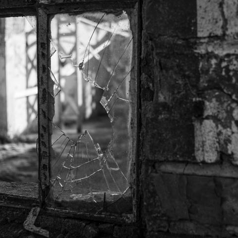 Eine Teilaufnahme von einem Fenster, wo das Glas in der Mitte zerbrochen ist. Das Foto ist in Schwarzweiß.