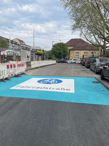 Straßenszene am Bahnhof Bad Cannstatt in Stuttgart. Auf dem Asphalt ist gut sichtbar das Piktogramm einer Fahrradstraße aufgebracht – weißes Fahrrad-Symbol mit Fahrbahnmarkierung. Es fehlen noch Verkehrszeichen.