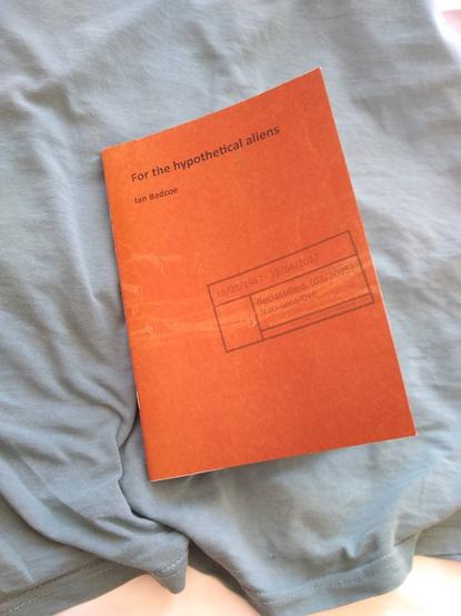 Cover of a poetry pamphlet, the title is "For the hypothetical aliens".  It is orange and worn, like an old document folder, and it has some sort of security stamp declaring the contents top have been reclassified "Non sensitive"