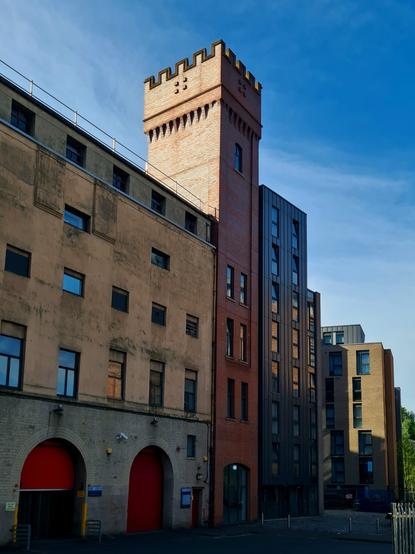 A Romanesque brick tower sandwiched between two more modern buildings.