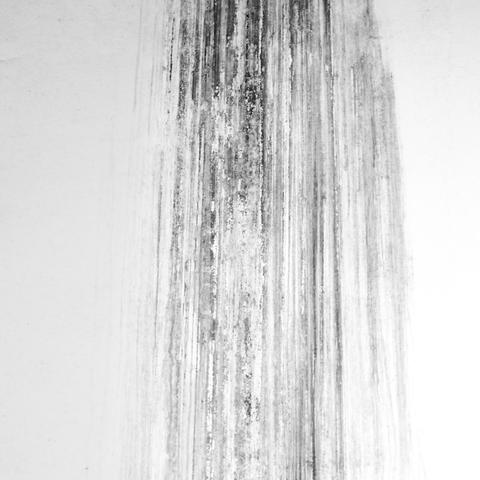 Dunkle Streifen auf einer weißen Wand. Sie stammen von einer defekten Regenrinne. Das Foto ist in Schwarzweiß.