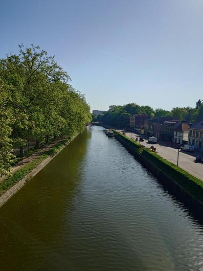 The river from the bridge. Some stationary boats, a pedestrian alley on the left, a street and houses on the right.