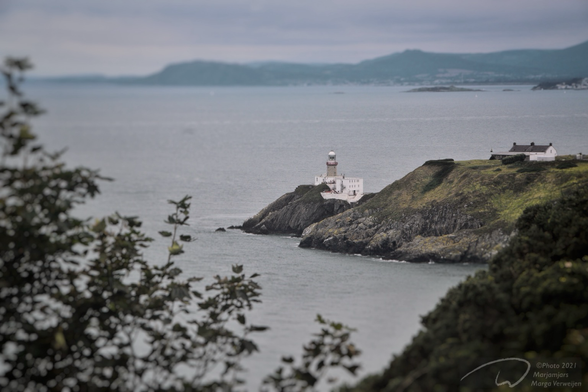 The Howth lighthouse seen through the bushes along the path over the cliffs by the sea.