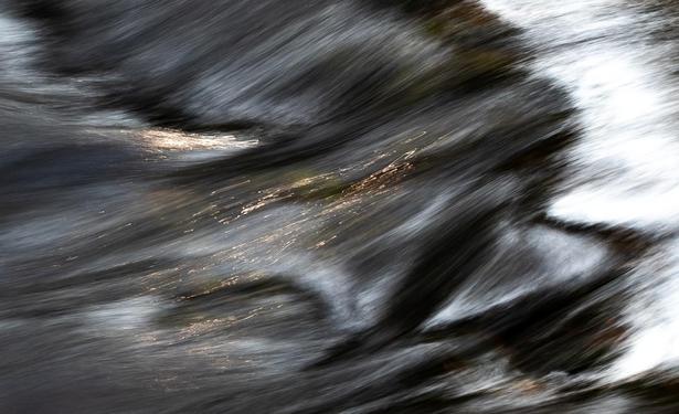 Looking down on a small section of stream. It is a long exposure so the bubbling bouncing stream has been smoothed. There is whitewater that is soft white and there is sunlight reflected on the water that looks like thousands of tiny fireflies.