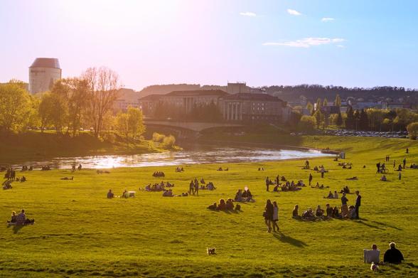 People sitting on a meadow by the river in small groups having picnic in the sun