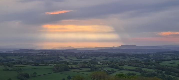 Early morning sun breaking through clouds, with shades of orange, peach and grey creating a striped appearance. Looking east towards Herefordshire from the foot of Black Hill.