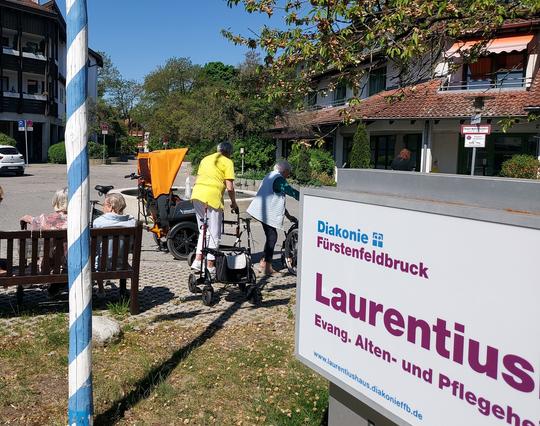 Amperrikscha vor dem Laurentiushaus in Olching. Davor stehen Rollatoren. Auf einer Bank warten Menschen auf die nächste Mitfahrt.