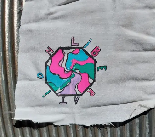 5-print screen printed patch. A slightly hypnotic swirl of different colours, flowing together within an octagon, on the outside of which the word 'Liberation' is written.