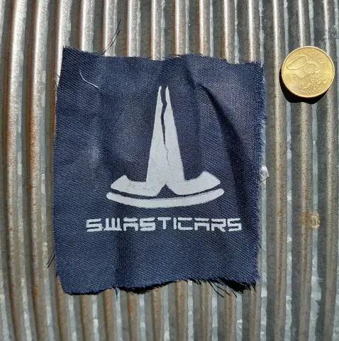 1-print screen printed patch (white on black). An upside down Tesla logo with a crack down the middle. Underneath, in the font of Tesla, is written: Swasticars.