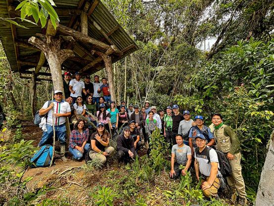 Große Gruppe von Exkursionsteilnehmer*innen in Outdoor-Kleidung versammelt unter einem Holzunterstand im dichten Regenwald von Chachapoyas, Peru
