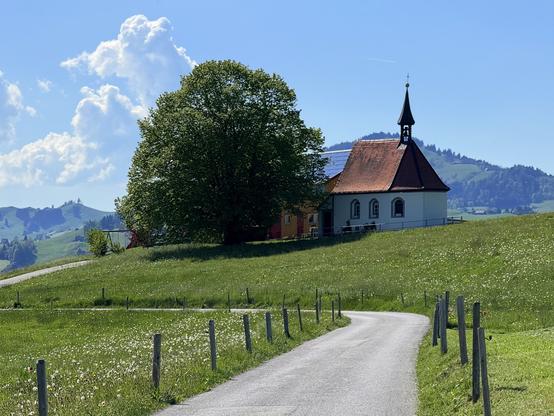 eine kappelle, ein baum und ein bauernhaus. und. die strasse dahin