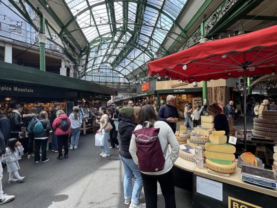 London market, with a cheese stall in the foreground; many wheels of cheese.