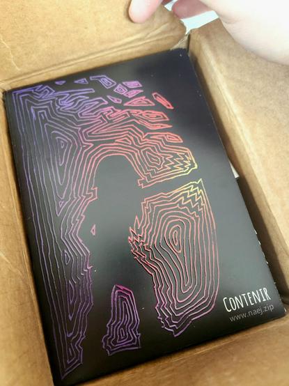 A box filled to the brim with prints of a design from Contenir the game