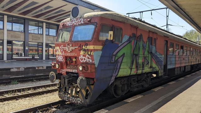 A red BDŽ class 32 EMU with lots of graffiti waiting in a railway station.