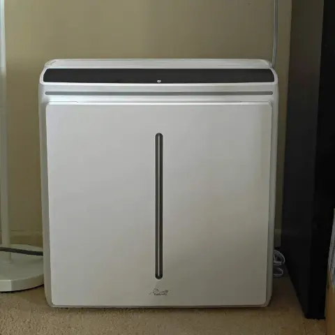 Sleek and modern air purifier with a touch screen display and a minimalist design, sitting elegantly on a wooden floor against a white wall.