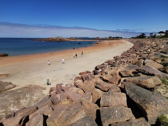 Un paysage de bord de mer. Une plage bordée de rochers au premier plan. Des îles en arrière-plan.