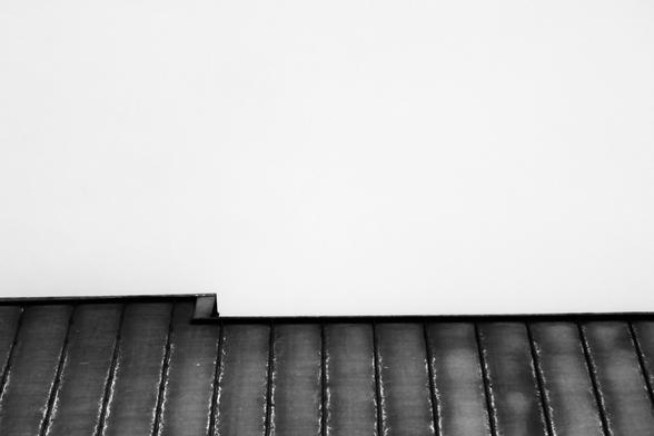 A black and white photo showing a low angle view of the roof line of a building. The roof line is not in alignment.