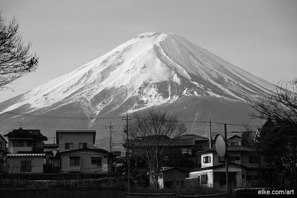 This timeless black-and-white photograph captures the majestic presence of Mount Fuji as seen from the charming village of Fujikawaguchiko.

The snow-capped peak rises powerfully above traditional Japanese houses and leafless winter trees, contrasting nature’s grandeur with everyday life. The absence of color emphasizes the graphic beauty of the scene, from the delicate textures of the mountain slopes to the silhouette of rooftops and power lines, blending serenity with subtle urban energy.

Perfect for minimalist and modern interiors, lovers of Japan’s landscapes, or fans of monochrome photography seeking quiet drama and sophistication.

Ideal for collectors of black and white photography, Japanese scenery, and serene mountain landscapes.
