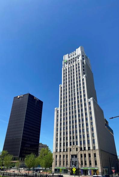Color image of two skyscrapers located in Akron, Summit County, Ohio, the PNC Bank Tower, c. 1969, steel and glass, and the Huntington Bank Tower, c. 1931, Art Deco, granite, limestone, and terra cotta. Image shows the two buildings soaring into a perfectly cloudless blue sky.