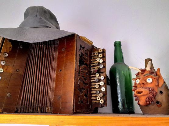 Sobre un acordeón diatónico de principios del S.XX un gorro de un abuelo, al lado una siempre viva botella de sidra (reciclable) y una ocarina de cerámica con ojos sorprendidos y cuernos. Todas tocan cantan y silban una vieja melodía…