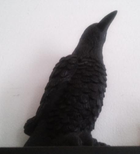 A figurine of a raven up on a shelf in front of a blank wall