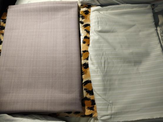 two bundles of fabric laid out next to each other on the very loud cheeta print plastic bag that they came in. the left fabric is a pink and white wool blend with a subtle plaid design. the right fabric is a beige and white striped cotton fabric.